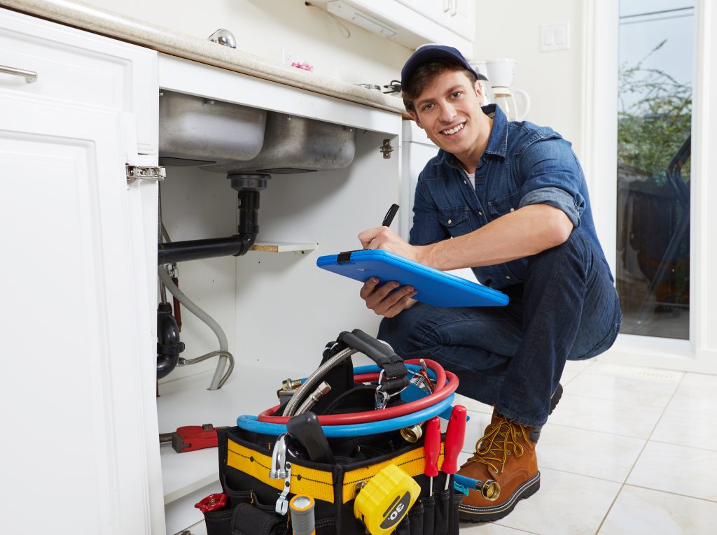 Plumber smiling as he is checking the pipe below the sink