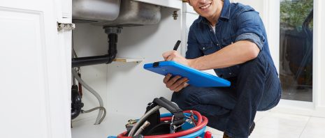 Plumber smiling as he is checking the pipe below the sink