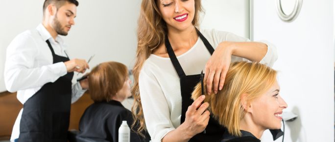 Smiling client sitting in a hair salon while hairdresser is combing her hair. Focus on client