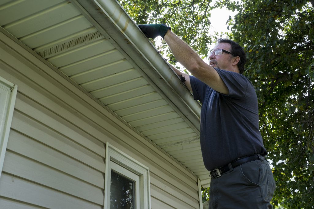 a man cleaning gutters on a house