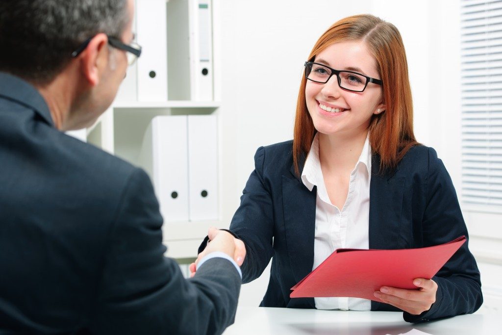 Man and woman shaking hands. Woman holding red folder in other hand