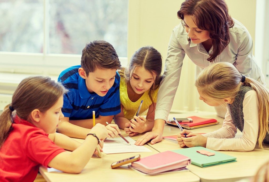 teacher helping school kids writing test in classroom