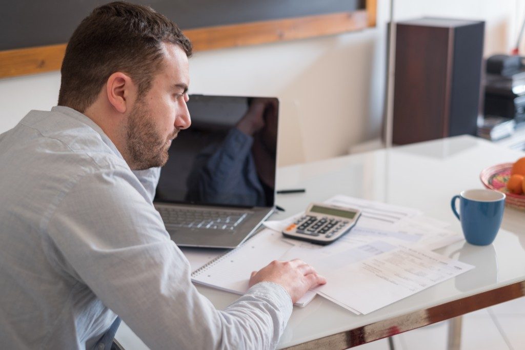 man computing with his laptop, calculator and documents